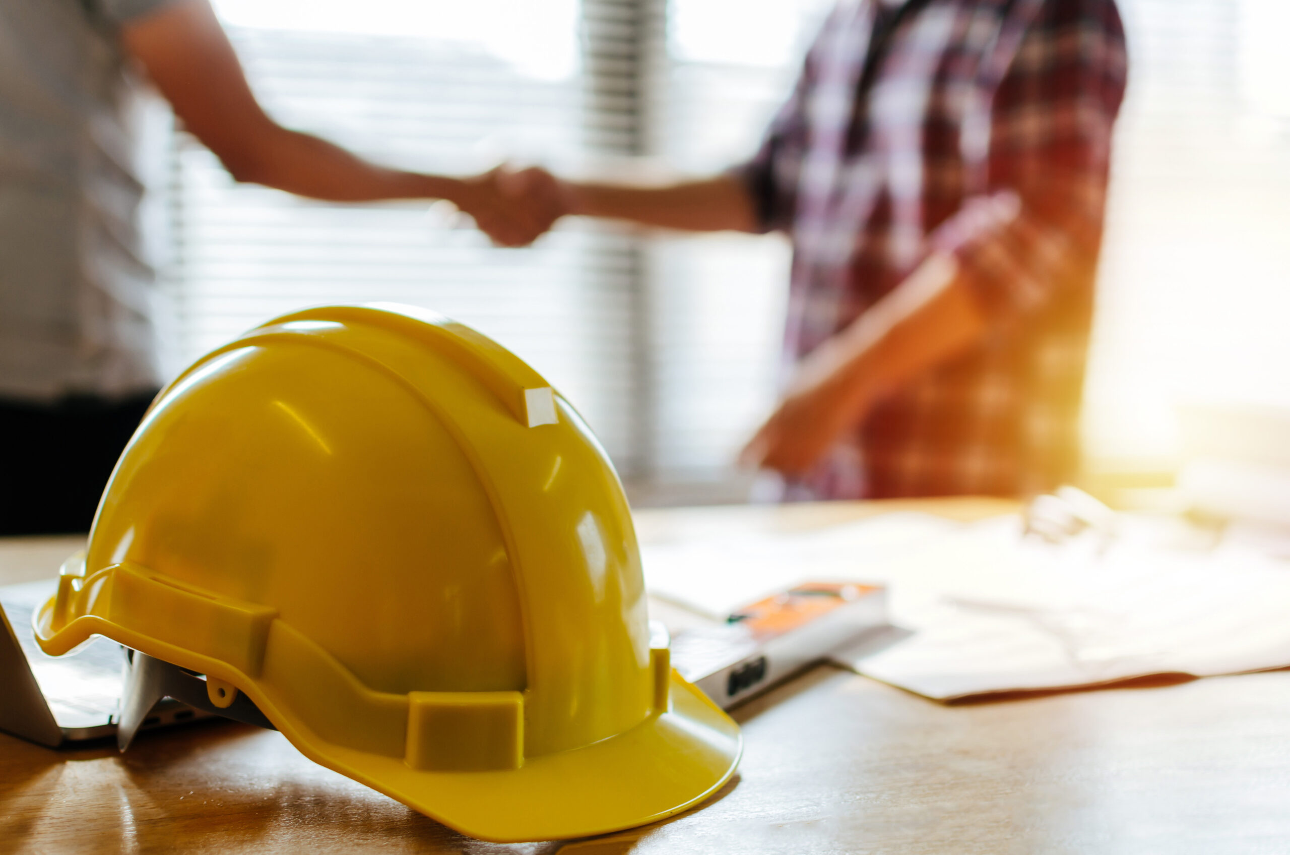 A yellow construction hard hat placed on a table with documents and a pen