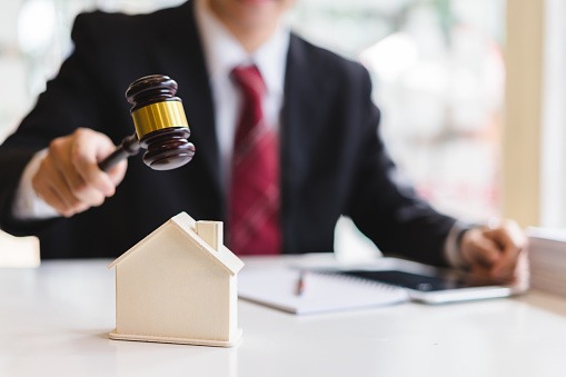 A model house sits in front of a judge's gavel, illustrating the legal aspects of housing and property law.